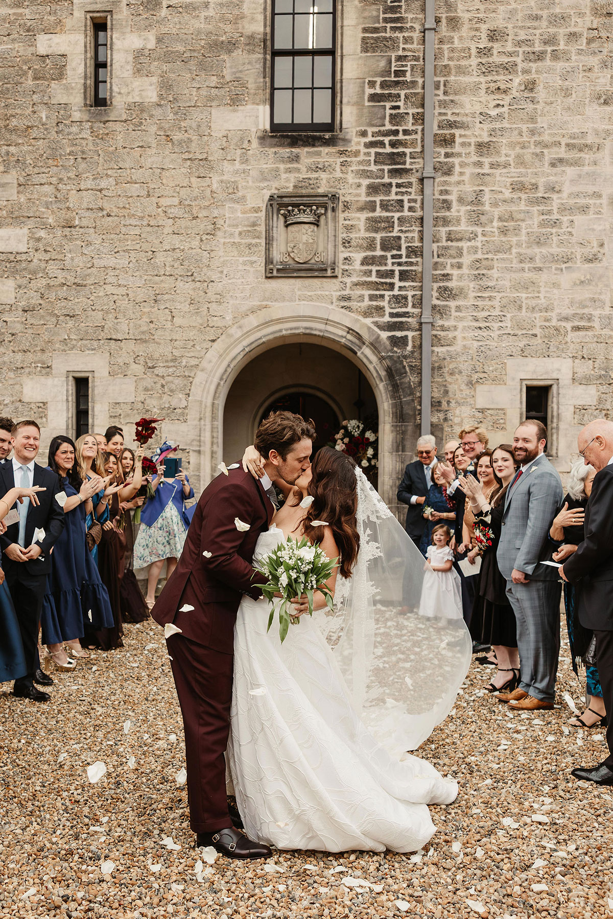 Bride and groom share a kiss during a confetti shower outside Barnbougle Castle, surrounded by wedding guests on the historic castle courtyard