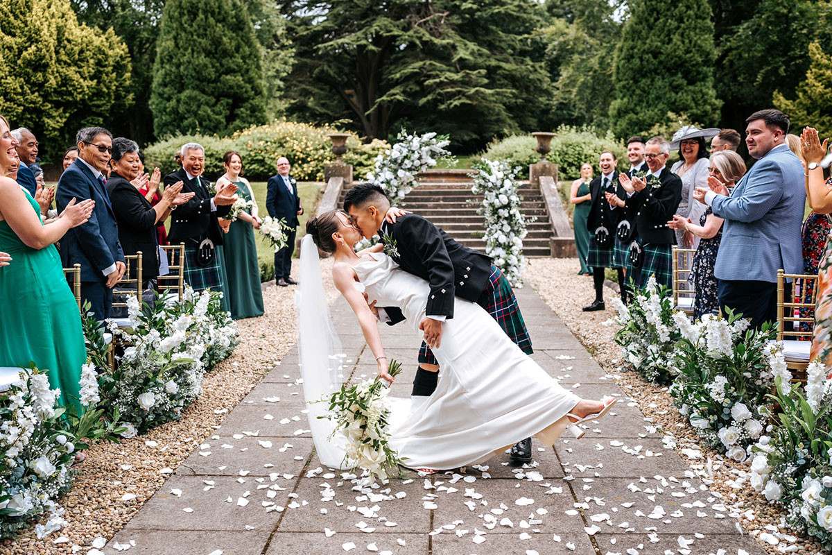 bride and groom kiss as guests cheer and throw confetti during wedding ceremony at mar hall