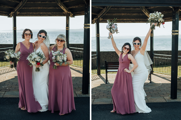 a bride and bridesmaids wearing dusky purple dresses wearing heart-shaped sunglasses having fun posing under a wooden pagoda at Seamill Hydro with sea in background