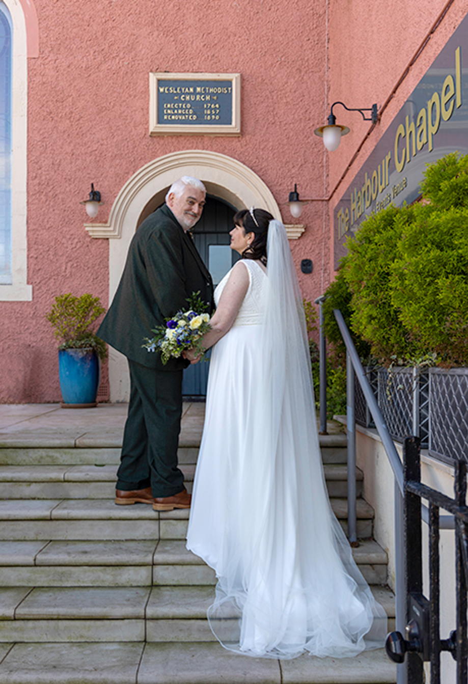 a bride and groom walking up a set of stone steps outside a pink coloured building