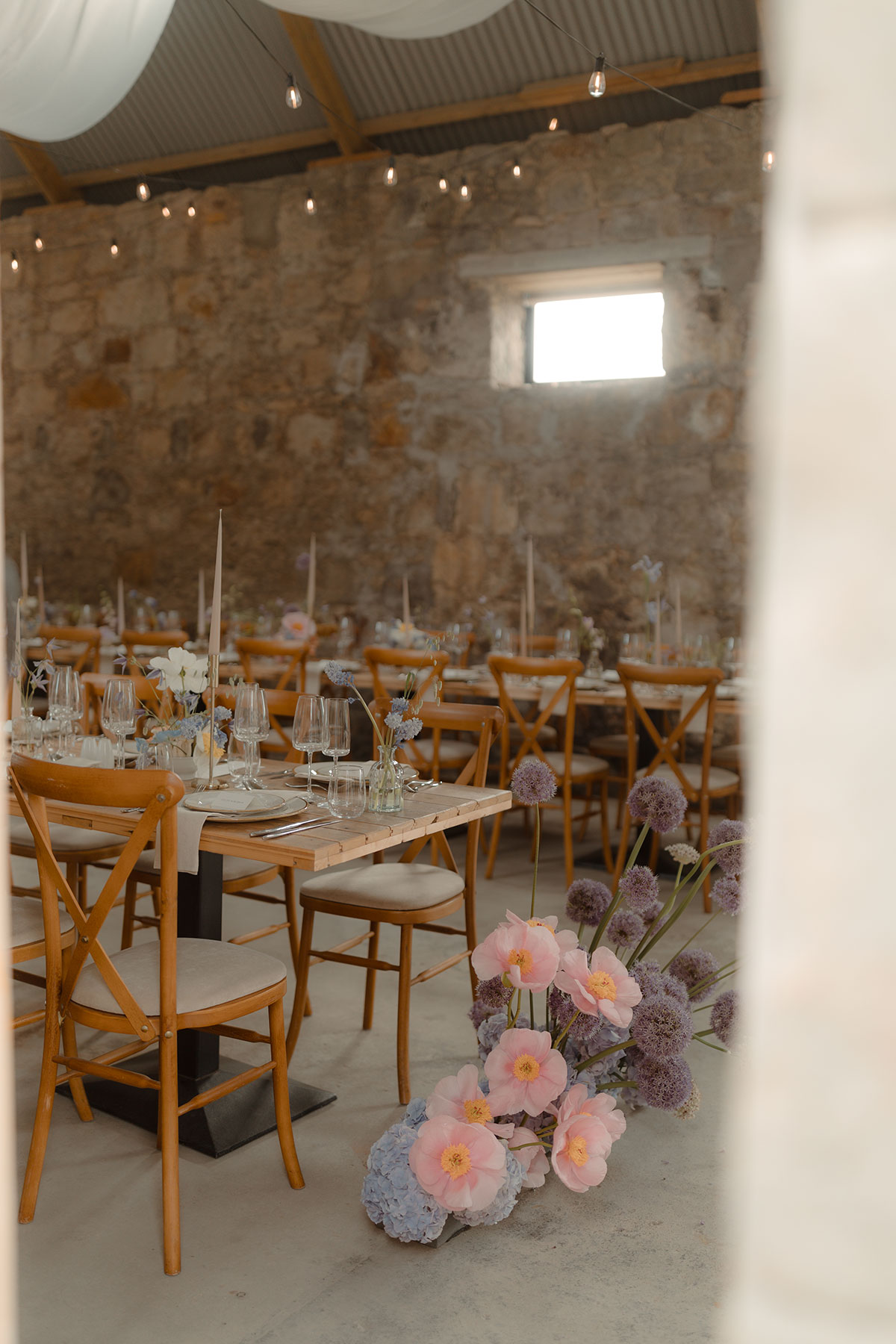Pastel wedding flowers beside wooden banquet tables inside rustic barn wedding venue near Falkirk, Scotland