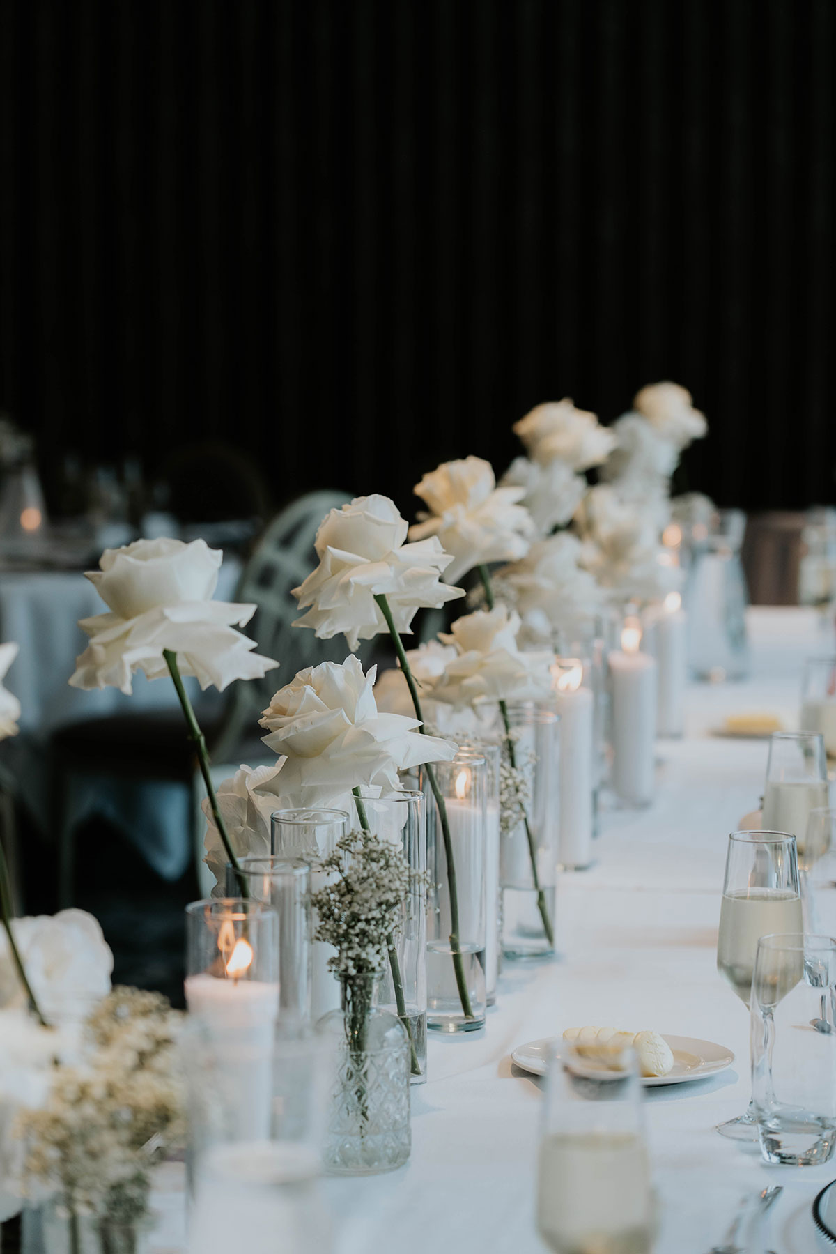 Monochrome wedding table styling with white roses in glass vases and candlelit place settings at Brisbane House Hotel