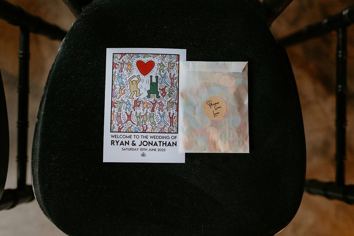 Colourful Keith Haring Wedding Invite And Confetti In White Paper Bag On Black Seat