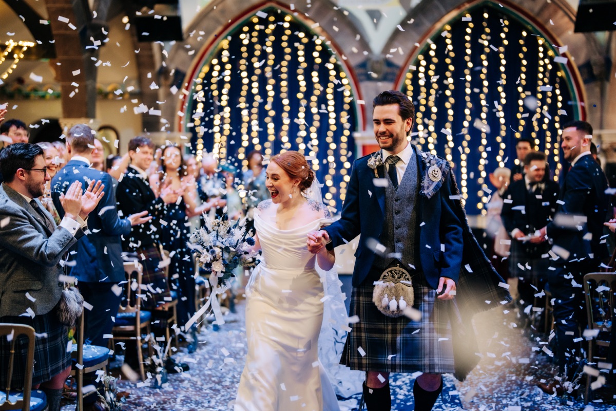 Newlyweds Robyn and James walk through a shower of white confetti as guests celebrate their wedding ceremony at Òran Mór in Glasgow.