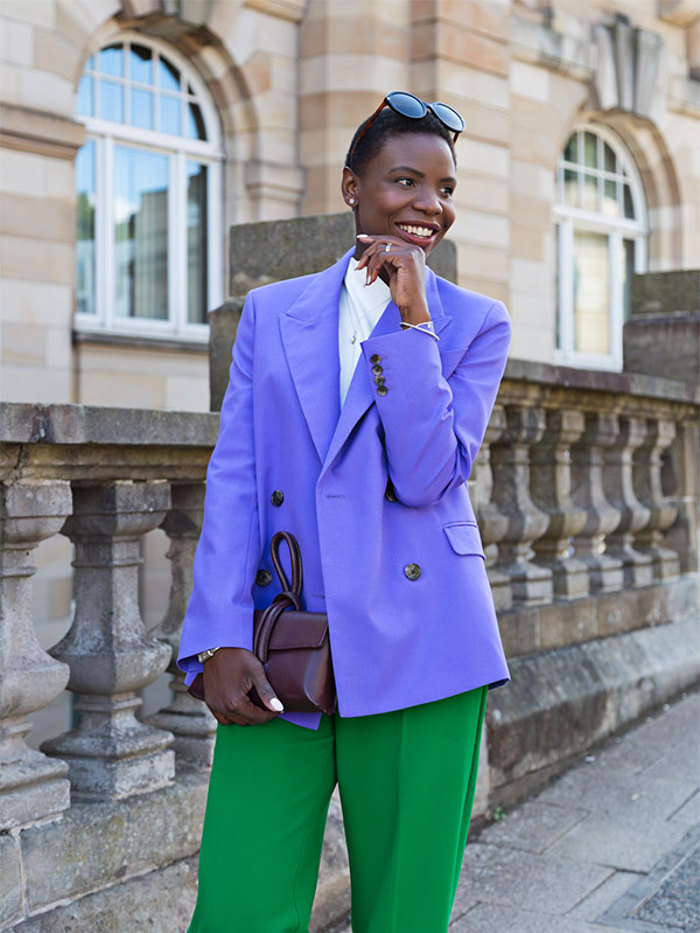 a woman smiles in a cityscape wearing a bold purple and green outfit