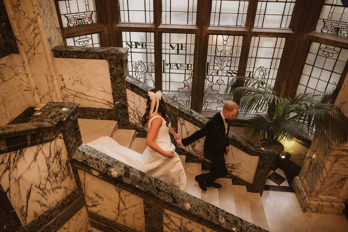 a bride and groom walking down a marble staircase in front of stained glass window at the Scotsman Hotel in Edinburgh
