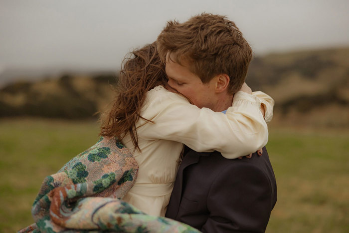 close up picture of bride wearing paisley print scarf hugging groom 