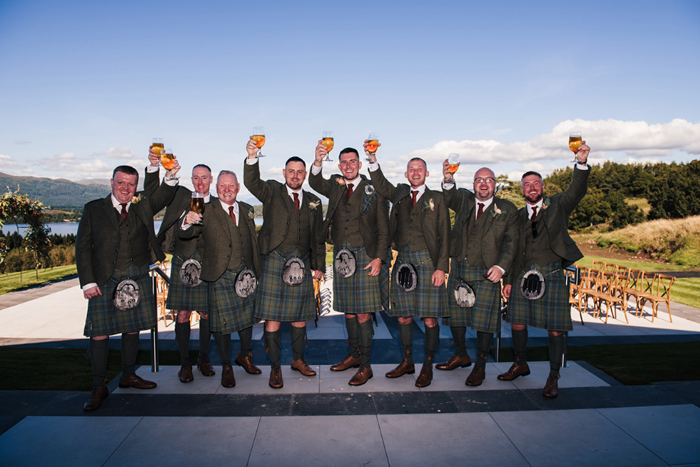 Groom and groomsmen all wearing kilts and toasting with pints of beer