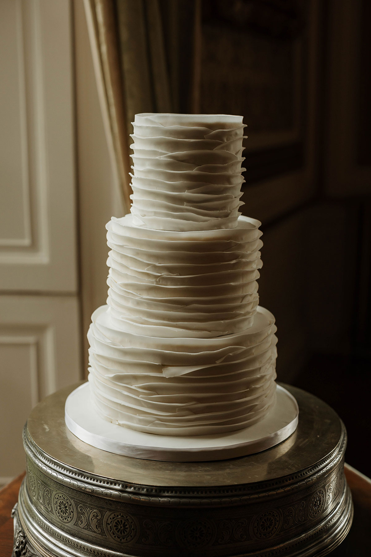 Three tier white rippled wedding cake on ornate stand at Drumtochty Castle Aberdeenshire reception