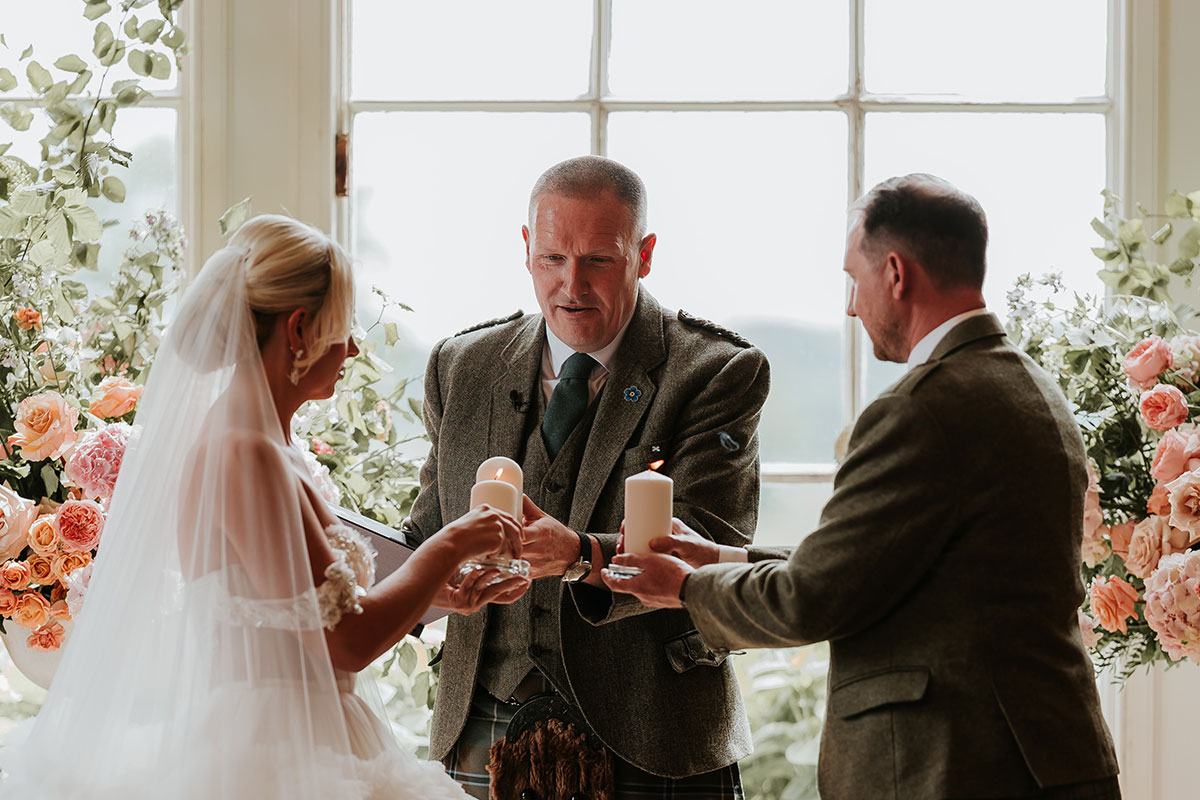 bride, groom and wedding celebrant all hold candles out in front of them for a ceremony ritual