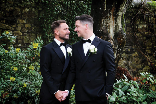 two grooms holding hands in the grounds outside Carlowrie Castle