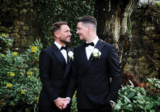 two grooms holding hands in the grounds outside Carlowrie Castle
