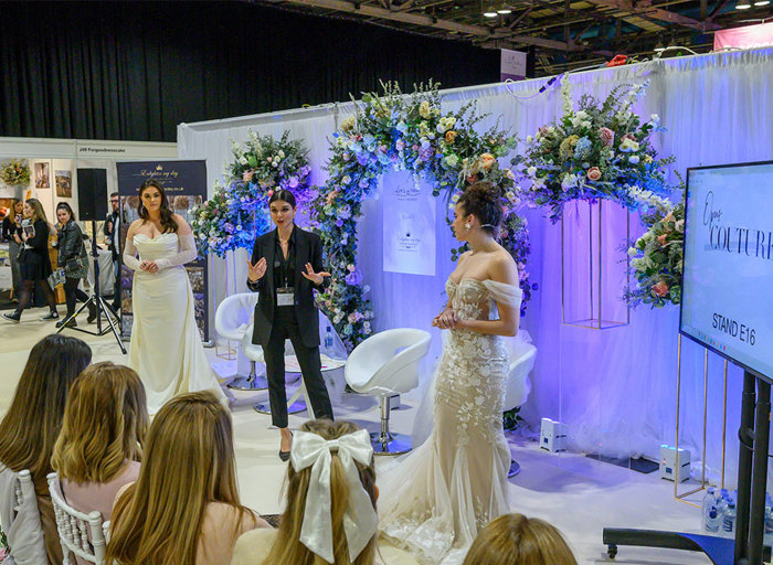 a woman in a black suit giving a presentation to a group of people with a woman in a wedding dress standing on either side of her