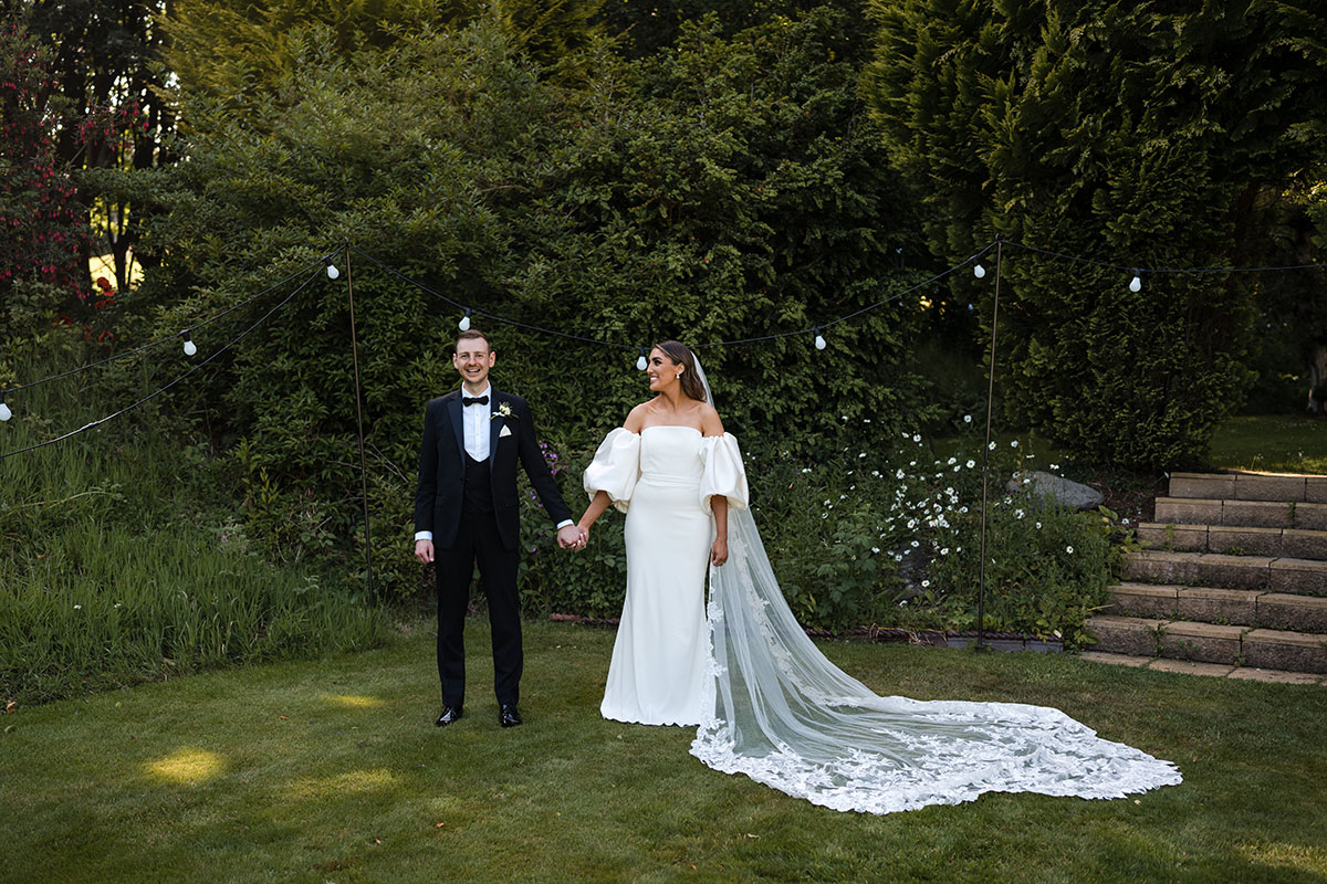 Bride looks at her groom smiling and holding hands in garden