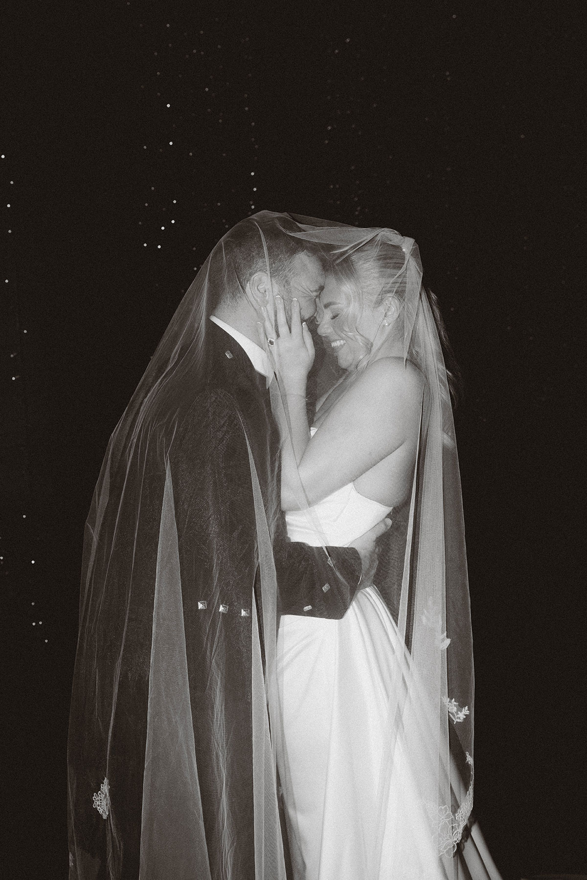 romantic black and white portrait of bride and groom under veil embracing