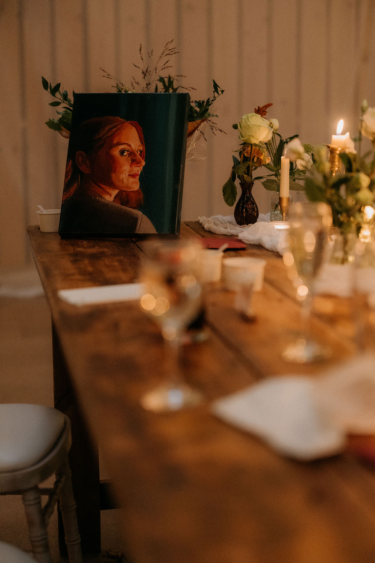 Wedding reception table detail with painted bridal portrait, candles and floral styling inside rustic barn venue