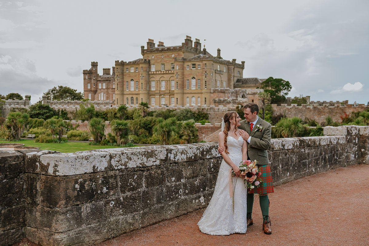 Bride and groom posing on the grounds of Culzean Castle with the historic castle and landscaped gardens in the background