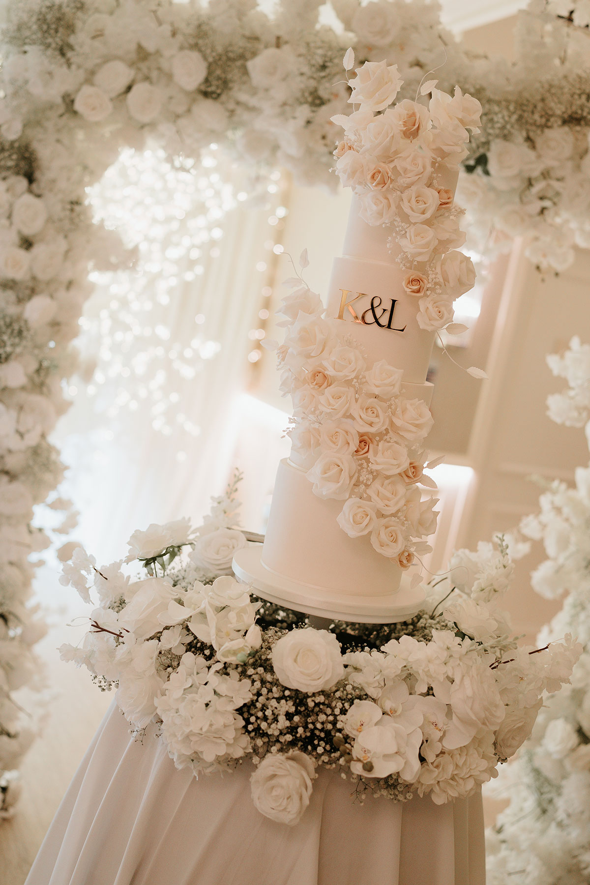 Four-tier white wedding cake with cascading rose decorations and gold initials at Ingliston Country Club