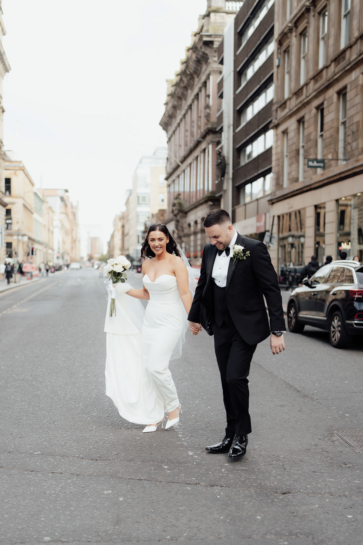 Bride and groom walking through city centre after civil wedding ceremony in Scotland