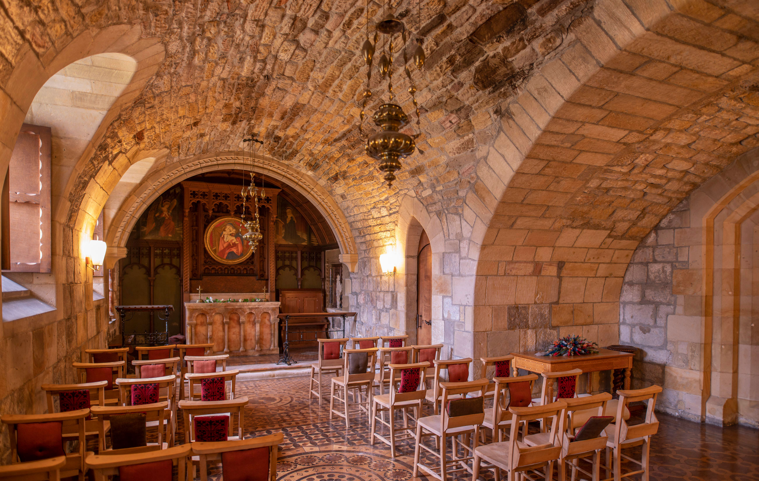 Newbattle Abbey chapel wedding ceremony space with stone vaulted ceiling, wooden chairs and historic altar in Midlothian