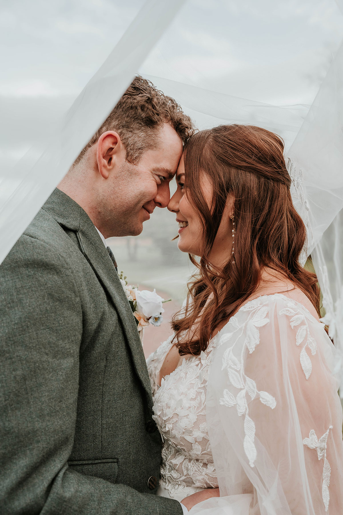 Close-up of the couple under the bride’s veil, touching foreheads 