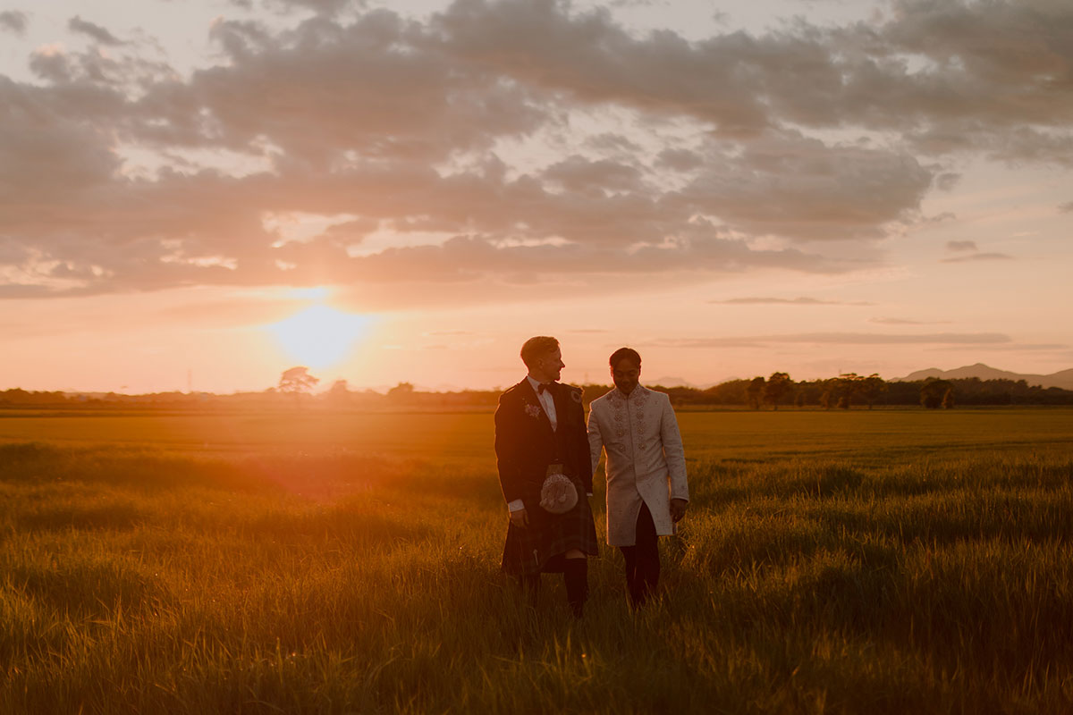Newlywed grooms walking through countryside field at sunset following Falkirk farm wedding