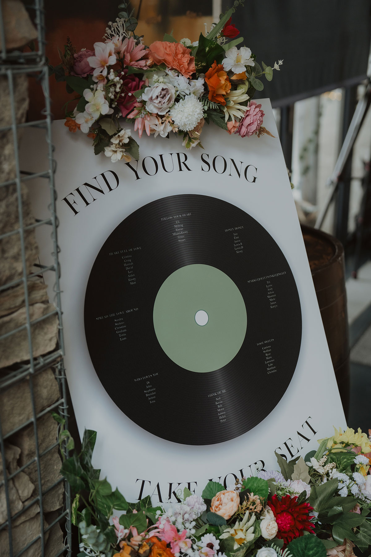 Vinyl record-style wedding seating plan sign surrounded by vibrant floral arrangements at modern Scottish wedding