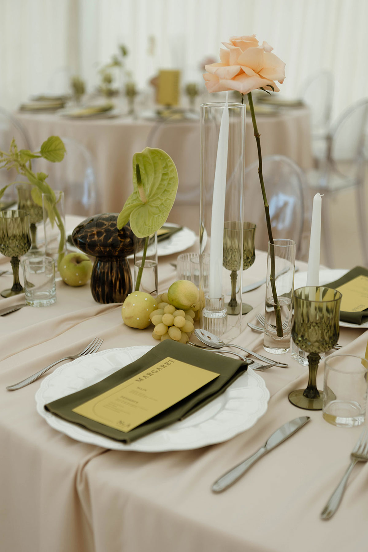 Close-up of modern wedding tablescape with green goblets, tall candles, fruit details and single-stem rose centrepiece.