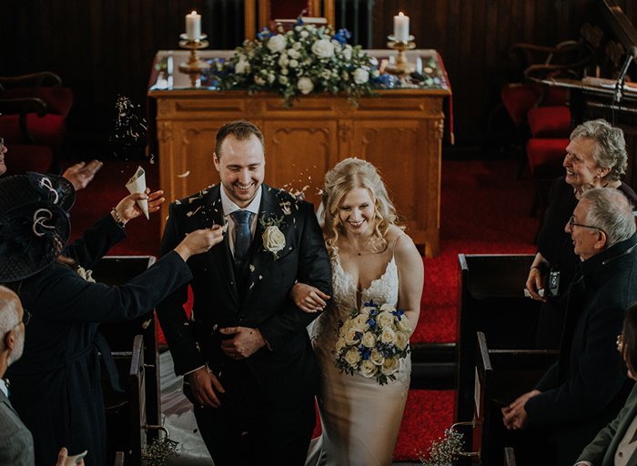 A bride and groom walking arm in arm out of a church as confetti is being thrown on them