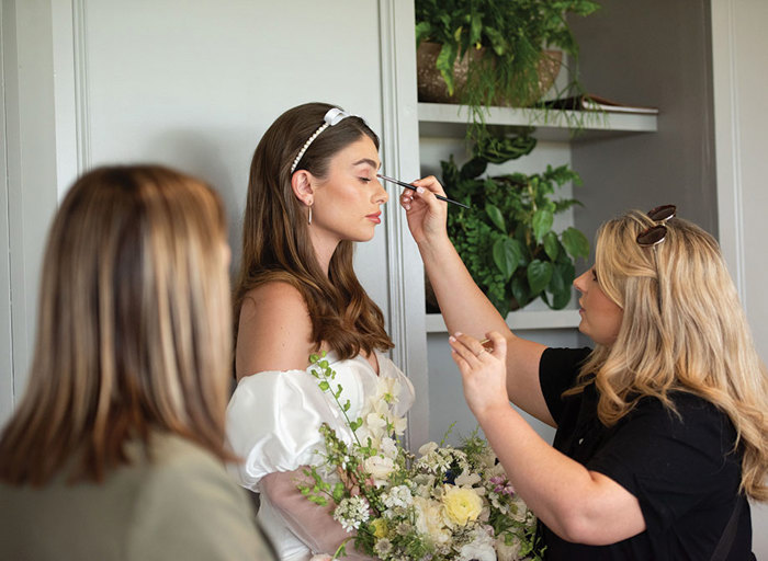 A woman applying eye makeup with a brush on a bride