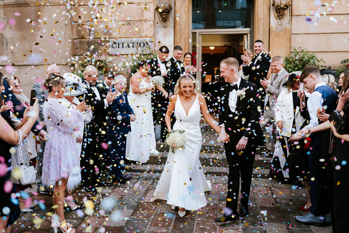 bride and groom exiting Citation onto cobblestone streets as people throw colourful confetti over them