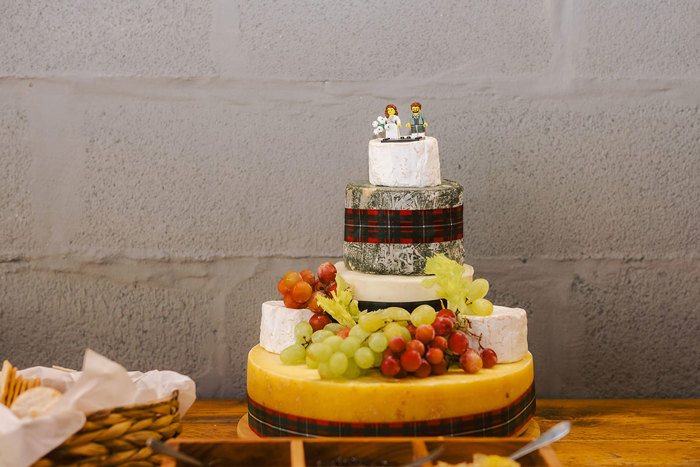 A wedding cake with two Lego figures on top and grapes at the bottom 