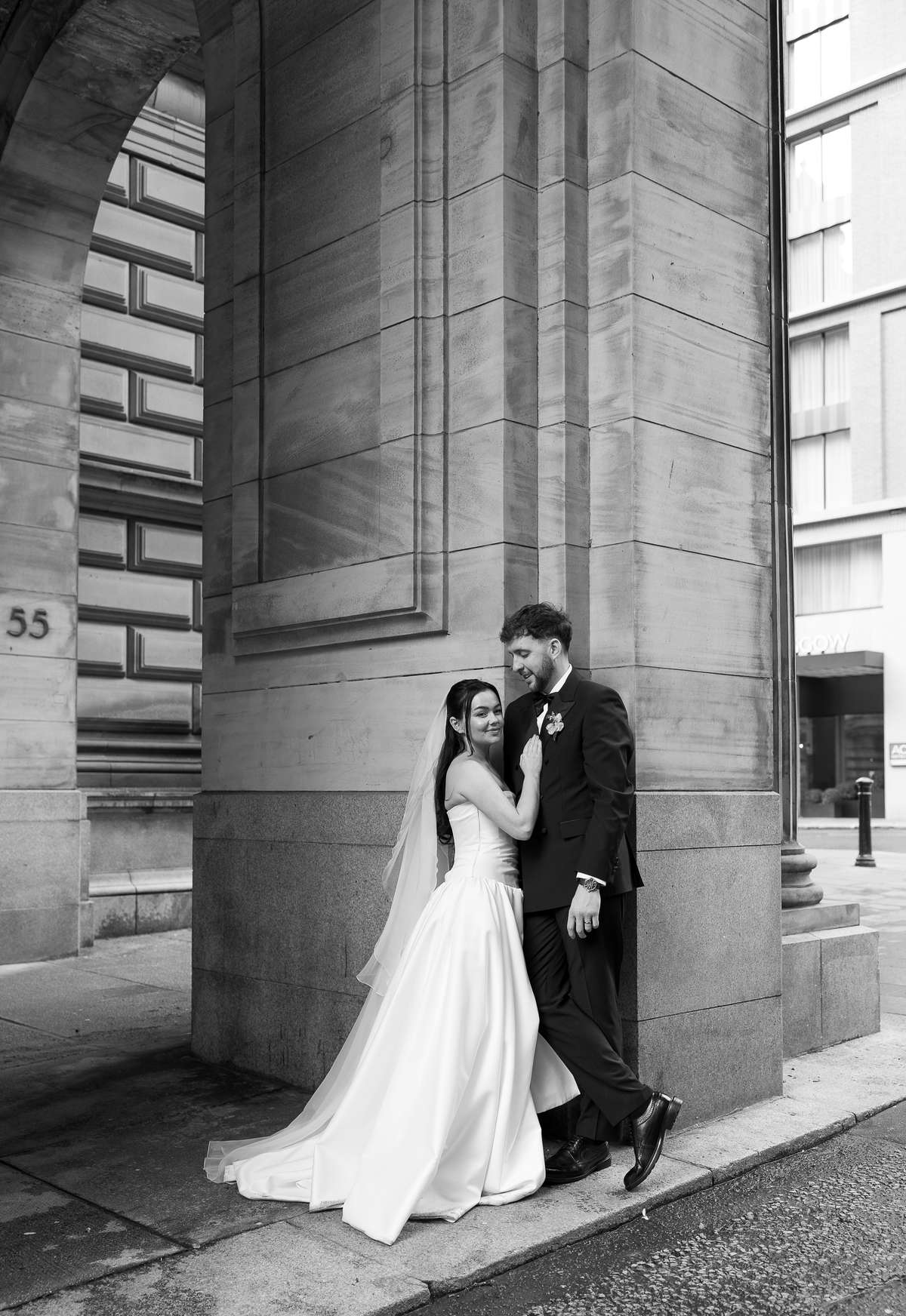 Bride and groom pose beneath the stone arches outside The Collector’s Hall during their stylish Glasgow city wedding.