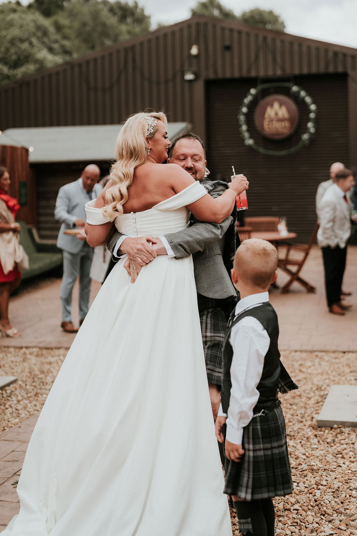 Groom lifts the bride in an embrace during the outdoor reception as a child looks on.