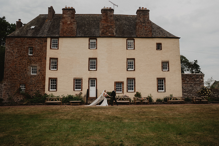 A Bride And Groom Walking Past The Exterior Of Wedderlie House
