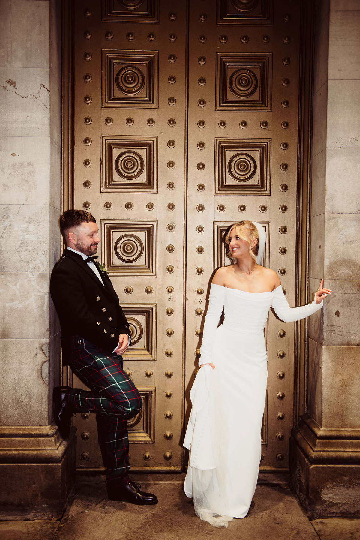 Bride and groom posing in front of large decorative gold doors, facing each other