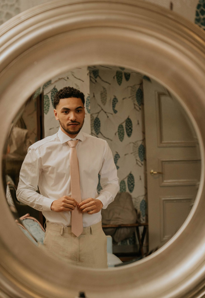 A man wearing a beige suit looking into a round mirror