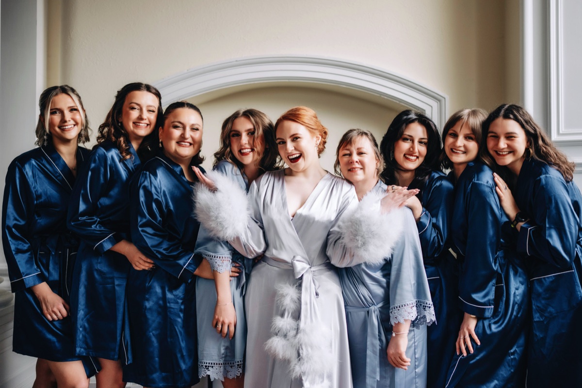 Bride Robyn poses with her bridal party wearing coordinated blue satin robes while getting ready for her Òran Mór wedding in Glasgow.