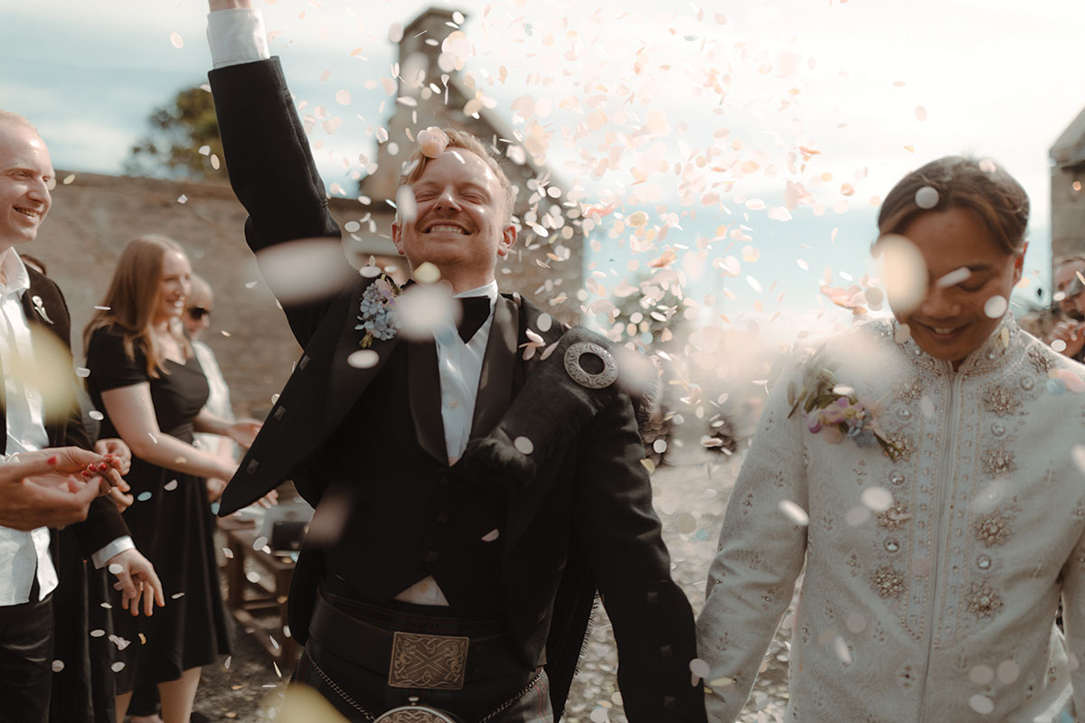Joyful confetti moment outside Falkirk farm wedding venue as grooms walk hand in hand after ceremony