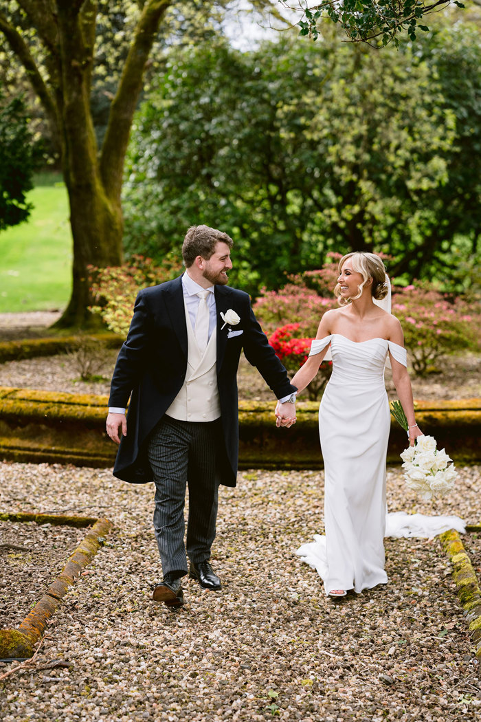 A bride and groom walking hand in hand in the gardens at Mar Hall.