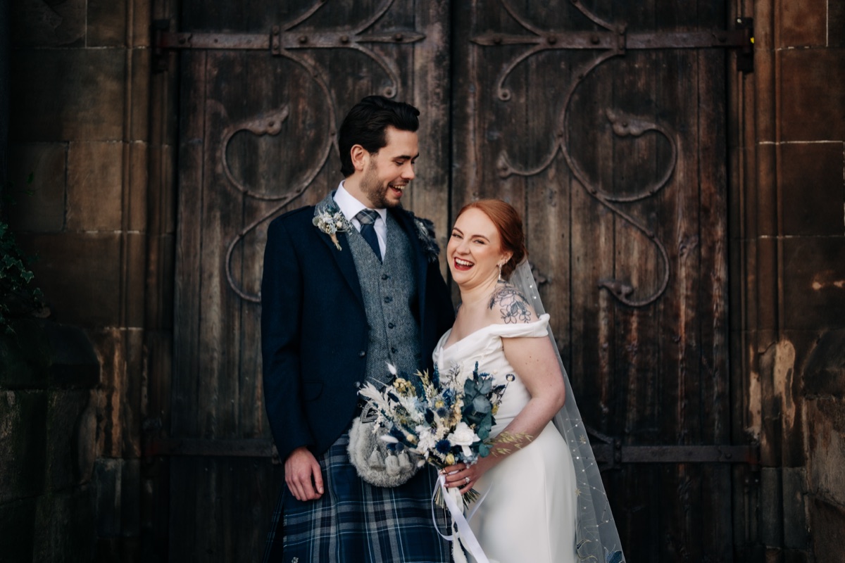 Robyn and James share a relaxed wedding portrait outside Òran Mór in Glasgow, wearing coordinating blue and grey tartan wedding outfits.