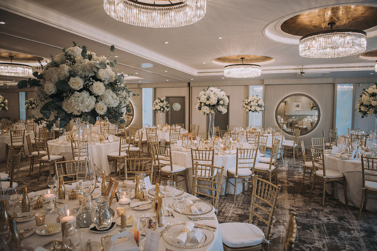 Lagavulin Suite at The Gailes Hotel & Spa set for a wedding reception with round tables, gold Chiavari chairs and tall floral centrepieces.