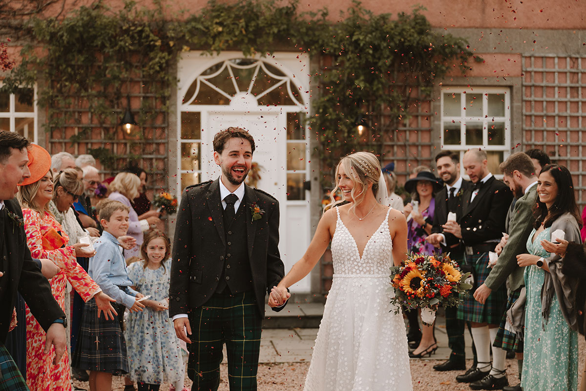 Bride and groom kissing outdoors after wedding ceremony with autumn trees in the background.