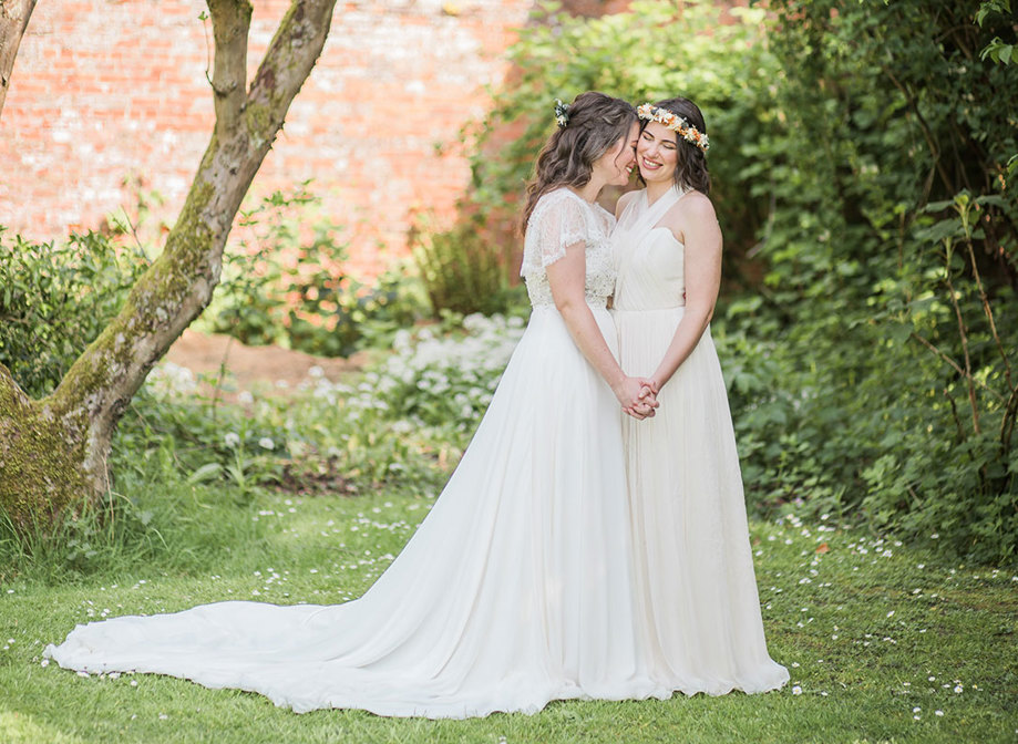 two brides wearing long and fluid wedding dresses standing romantically head-to-head in a walled garden setting at Byre at Inchyra