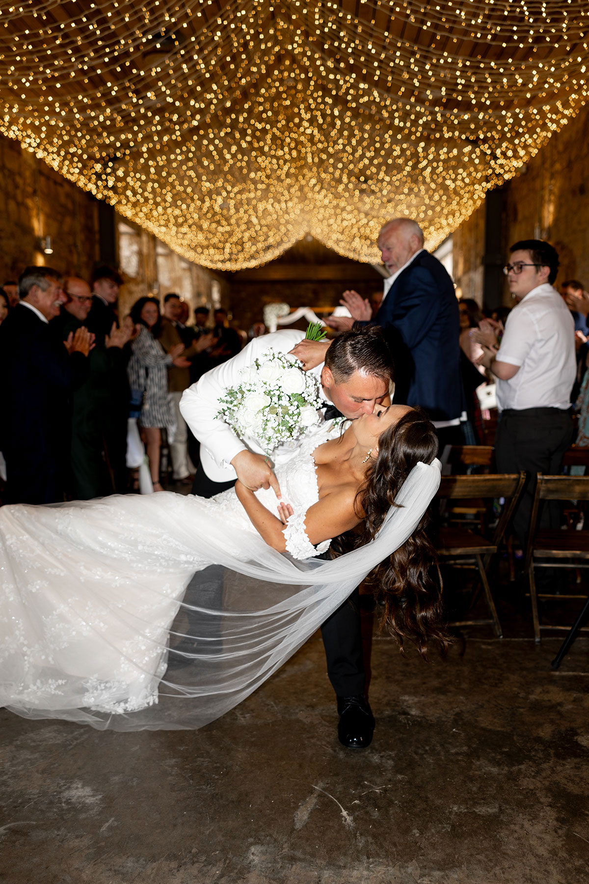 Groom dips bride for a kiss at the end of the ceremony beneath fairy lights at Falside Mill barn