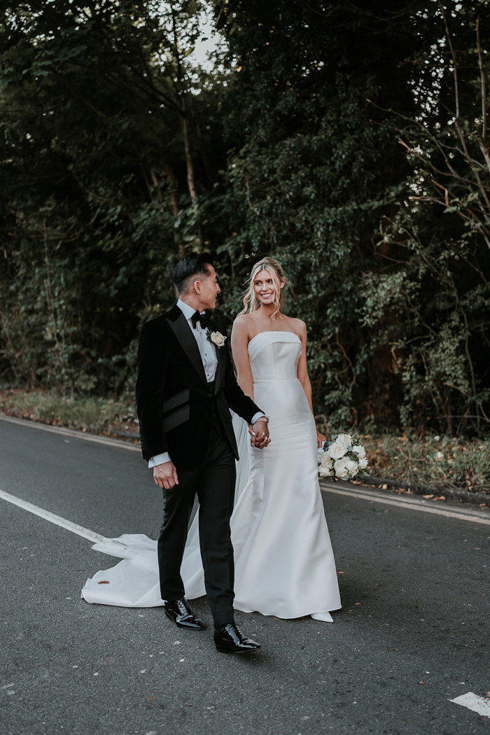 a bride and groom walking hand in hand along a road with trees behind them