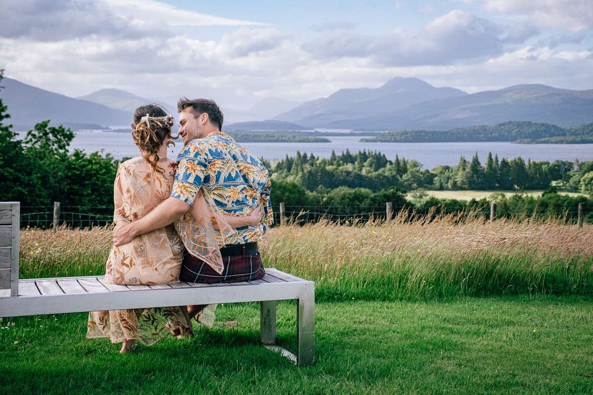 Newlyweds sitting together on a bench at Ardoch Loch Lomond looking towards the mountains