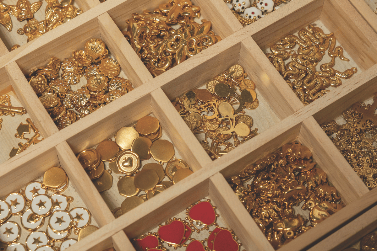 Selection of gold jewellery charms displayed in wooden compartments for creating personalised charm bracelets and necklaces.