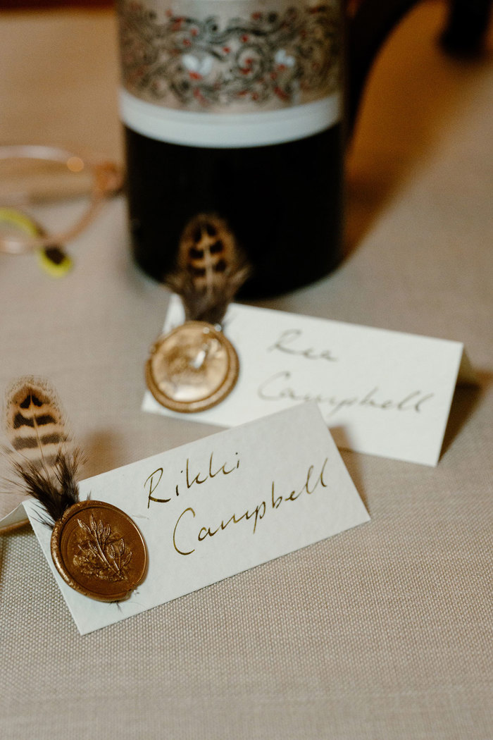 a cream card place setting with bronze wax seal and feather detail with calligraphy style handwriting 