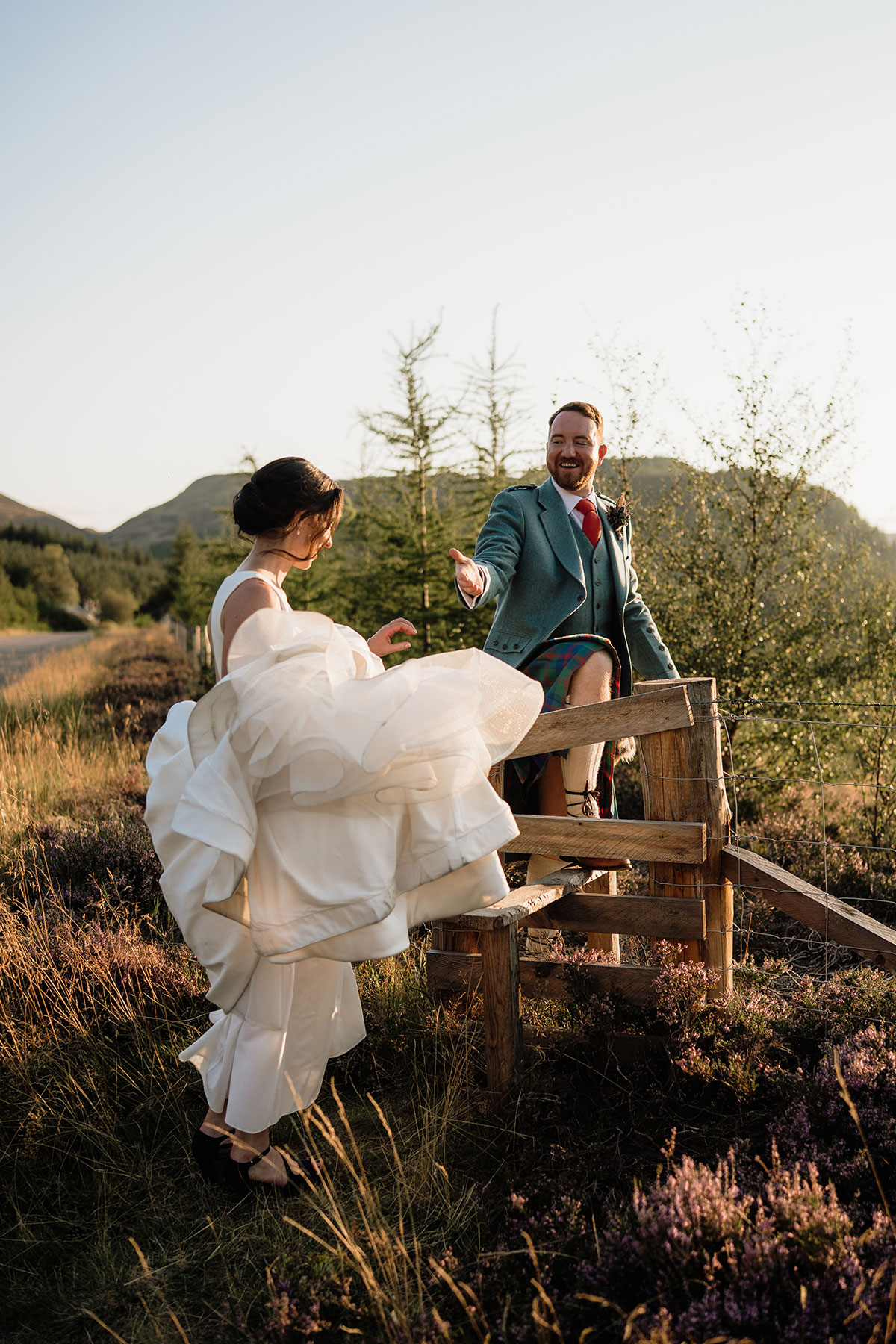 Bride climbing a wooden gate with help from the groom during sunset wedding portraits in the Cairngorms National Park